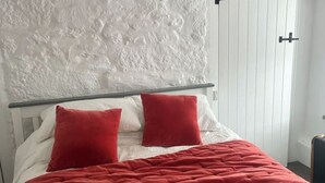 Un lit avec une couvre-lit rouge matelassée et deux oreillers rouges, une tête de lit blanche et un mur blanc à texture.