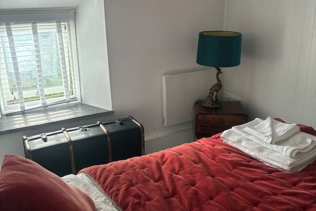 A bedroom with a bed, a suitcase, a lamp, and a window with blinds.