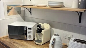 Une cuisine équipée d’un four à micro-ondes, d’une machine à café, d’un grille-pain et d’une étagère où sont rangées des assiettes et des tasses.