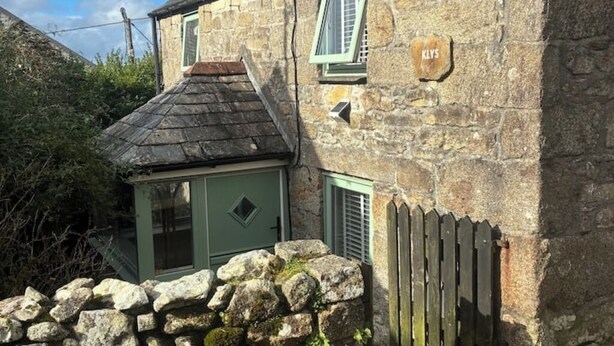Une maison en pierre avec une porte et des volets verts, un petit porche et une clôture en bois.