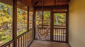 A hammock hanging in a wooden deck area with large windows overlooking a forested area. - Mountain View Escape-Dog friendly, Screened Porch (Dahlonega)