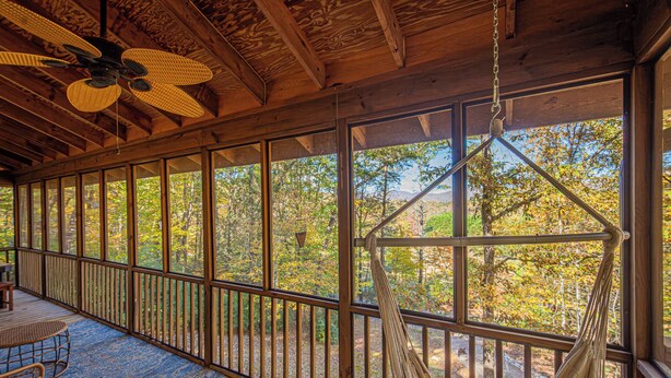 A wooden deck with a hammock, a ceiling fan, and a view of trees through large windows. - Mountain View Escape-Dog friendly, Screened Porch (Dahlonega)