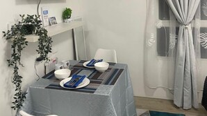A dining area with a table set for two, a flat-screen TV mounted on the wall, a small plant on a shelf, and a window with curtains. - Modern Studio Retreat at Mesavirre Residences (Bacolod City)