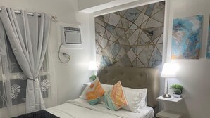 A neatly arranged bedroom with a bed, bedside tables, and a wall-mounted air conditioner. - Modern Studio Retreat at Mesavirre Residences (Bacolod City)