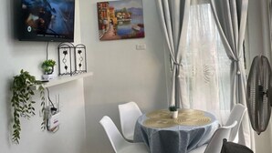 Un salon moderne avec un téléviseur à écran plat, un tableau, une table à manger avec des chaises, un luminaire au plafond et une fenêtre avec des rideaux.