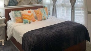Une chambre d’hôtel avec un lit, une table de chevet, une lampe, un tableau au mur et une fenêtre avec des rideaux.
