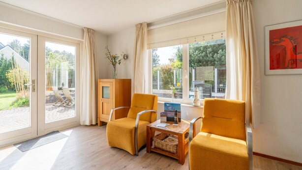 A room with two yellow armchairs, a wooden table, and a view of the outdoors through large windows. - Charming Villa Near the sea and Forest (De Koog)