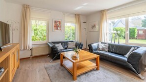A living room with two black leather sofas, a wooden coffee table, and a TV on a wooden cabinet. - Charming Villa Near the sea and Forest (De Koog)