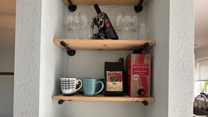 Una cocina con estantes de madera que sostienen copas de vino, una cafetera y una caja de café Bota Box.