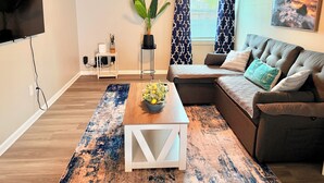 Ein modernes Wohnzimmer mit einem Ecksofa, einem Couchtisch, einem Fernseher und einem Deckenventilator.