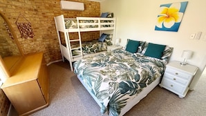 A room with a bunk bed, a desk, a nightstand, and a tropical-themed bedspread. - Ocean Shores Apartment 3 (South West Rocks)