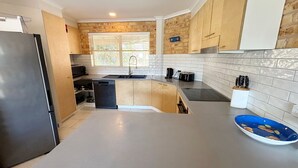 A kitchen with a stainless steel refrigerator, a dishwasher, a sink, and a countertop with a blue bowl. - Ocean Shores Apartment 3 (South West Rocks)