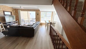 A living room with a sofa, a TV, and a dining area with chairs and a table. - Ocean Shores Apartment 3 (South West Rocks)