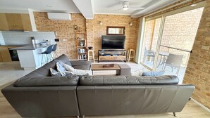 A modern living room with a leather sofa, a TV, and a bookshelf. - Ocean Shores Apartment 3 (South West Rocks)