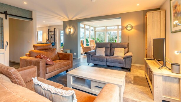 A spacious living room with leather sofas, a coffee table, and a TV on a wooden stand.