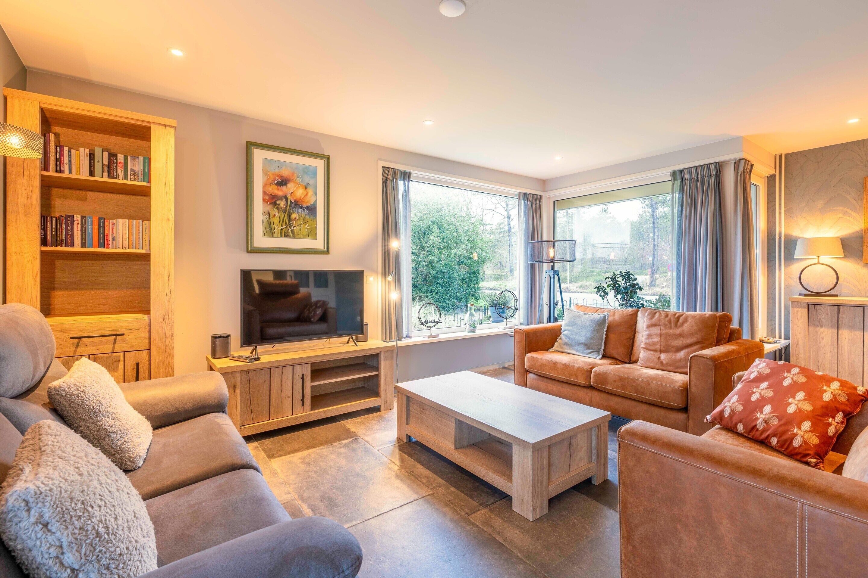 A modern living room with a sofa set, a coffee table, a TV, a bookshelf, and a large window with curtains.