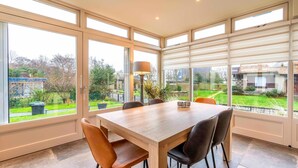 A dining area with a large table and chairs, large windows with blinds, and a view of the outside.