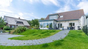 A modern house with a large glass conservatory, a paved driveway, and a well-maintained lawn.