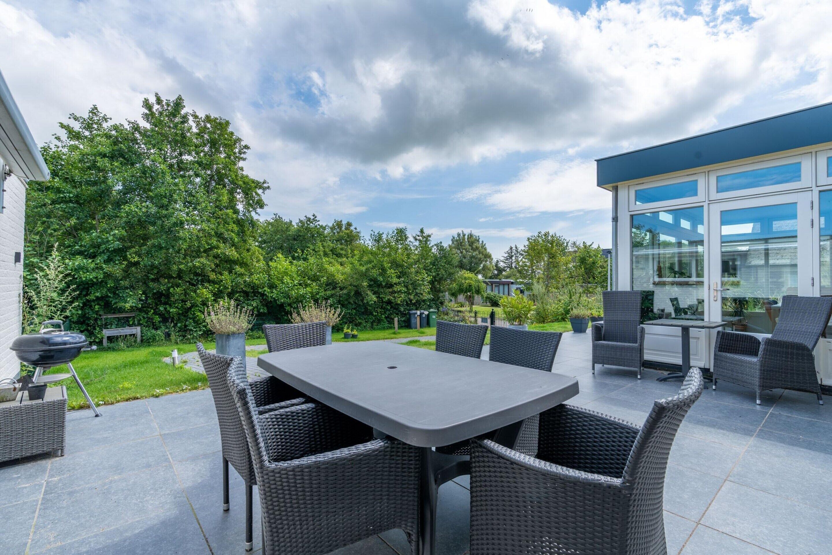A patio area with a table and chairs, a barbecue grill, and a glass-enclosed kitchen area.