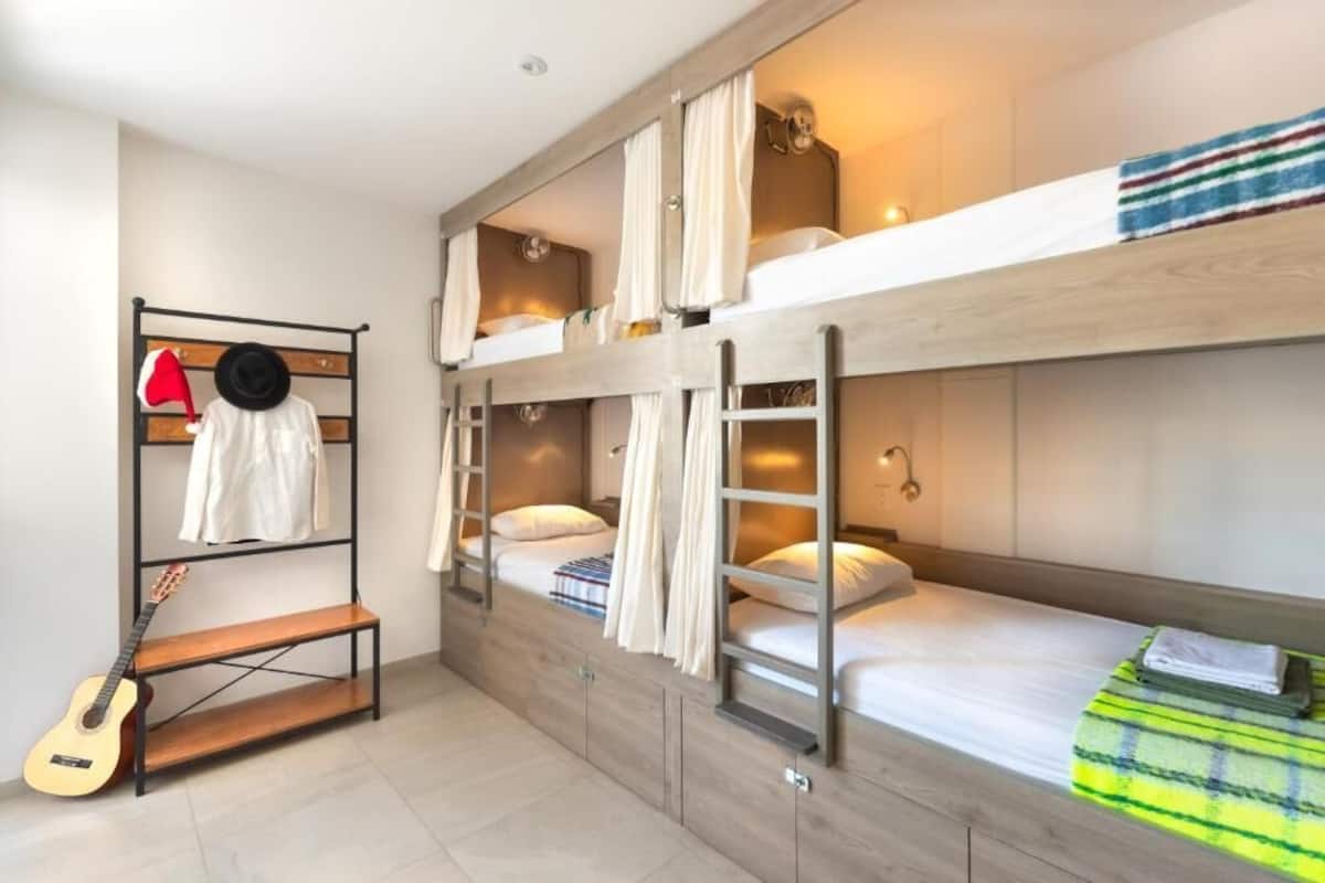 Habitación con literas, una guitarra, un banco y un perchero.