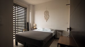 Een slaapkamer met een bed, nachtkastjes, een wanddecoratie met een droomvanger en een raam met jaloezieën.
