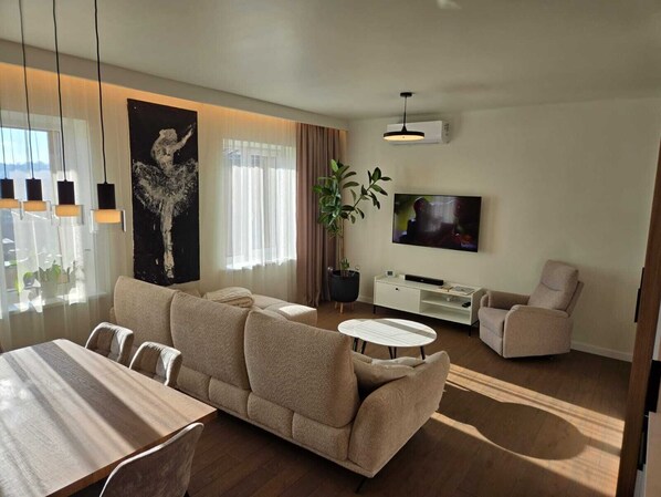 A modern living room with a sofa, a dining table, a TV, and a potted plant.