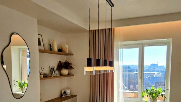 Een eetgedeelte met een houten tafel en stoelen, een hanglamp, een spiegel en een raam met uitzicht.