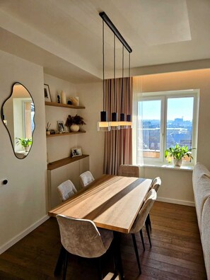 Ein Essbereich mit einem Holztisch und Stühlen, einer Pendelleuchte, einem Spiegel und einem Fenster mit Blick.