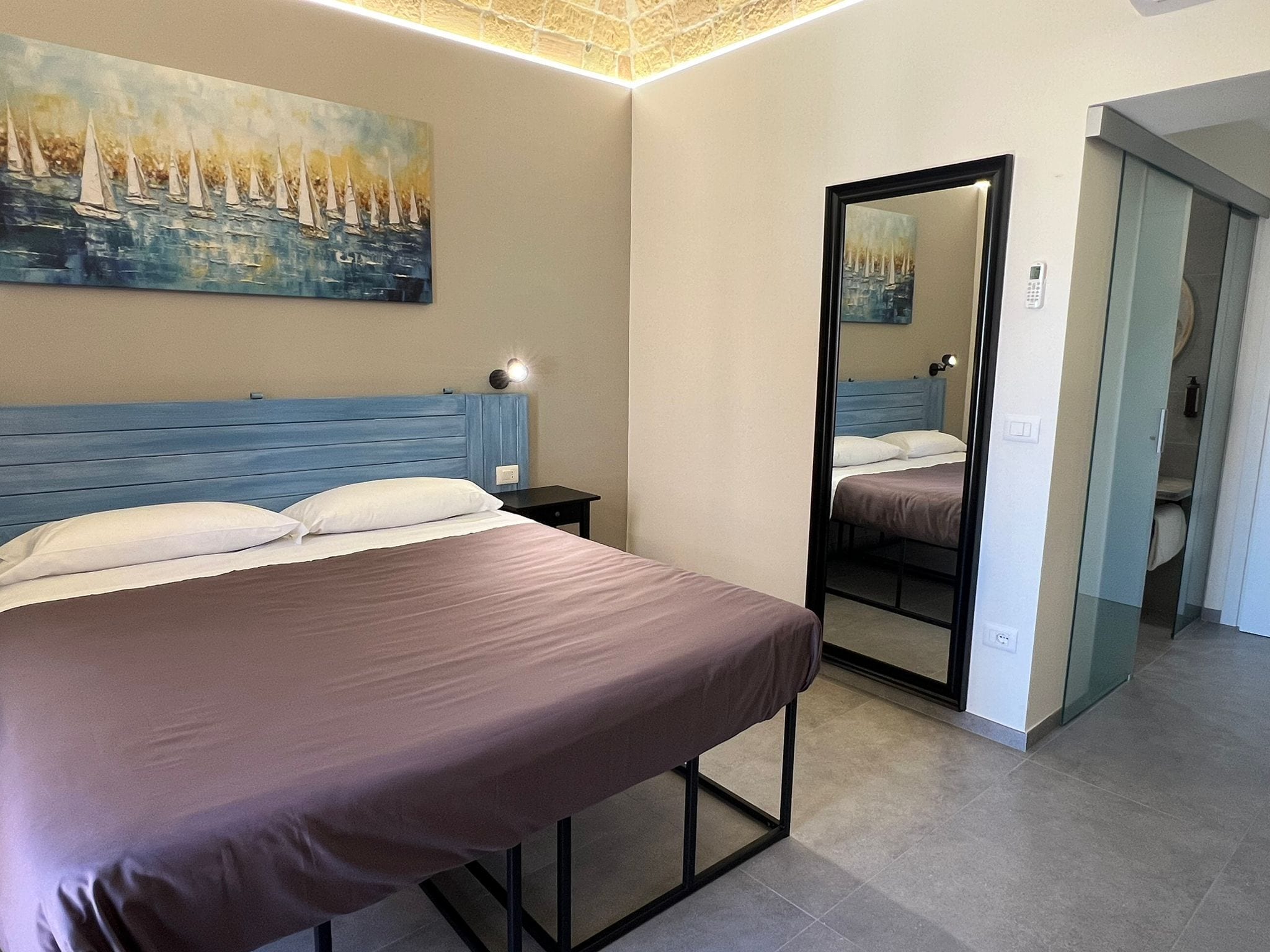 A bedroom with a bed, a nightstand, a painting, and a mirror.