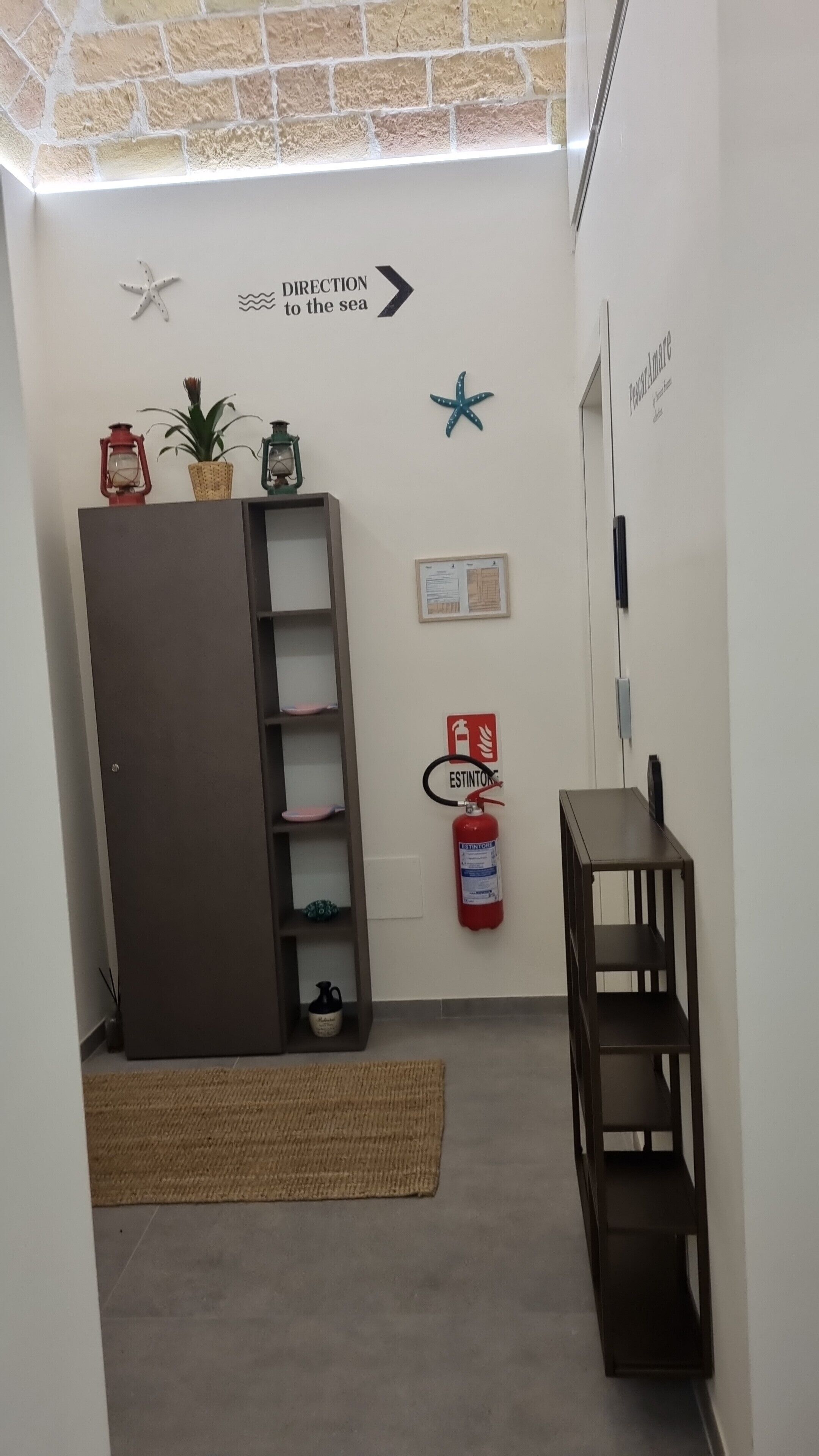 A hallway with a directional sign to the sea, a fire extinguisher, a wooden cabinet, and a small table.