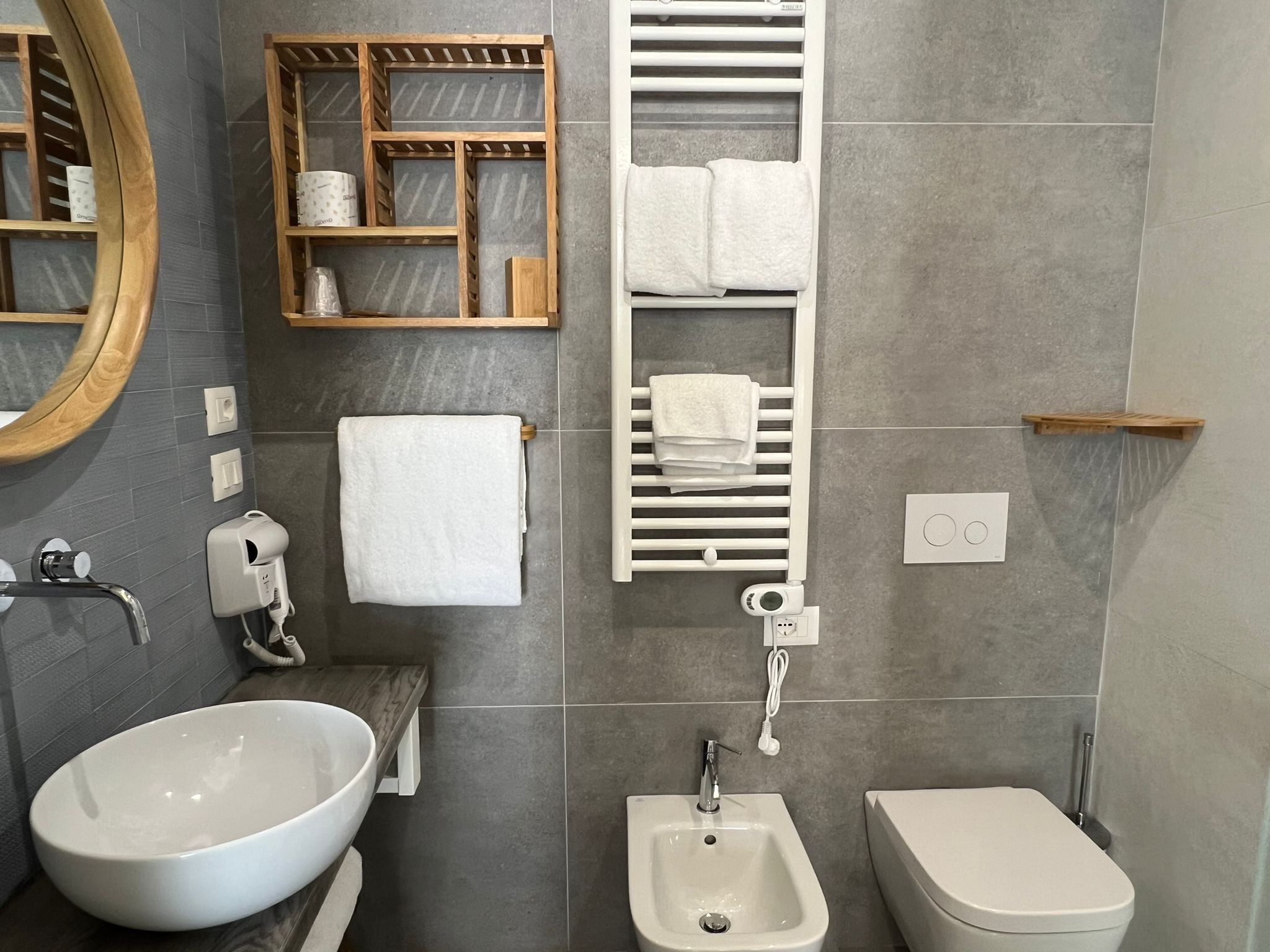 A modern bathroom with a large oval sink, a bidet, a toilet, a mirror, and a towel rack.