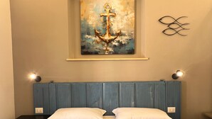 Un dormitorio con cama, dos lámparas de noche, una obra de arte colgada en la pared con un ancla y un cabecero azul.