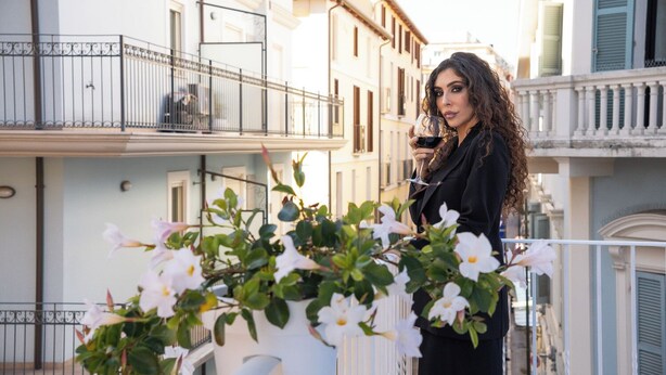 Un balcón con flores blancas, una barandilla y un edificio con balcones al fondo.