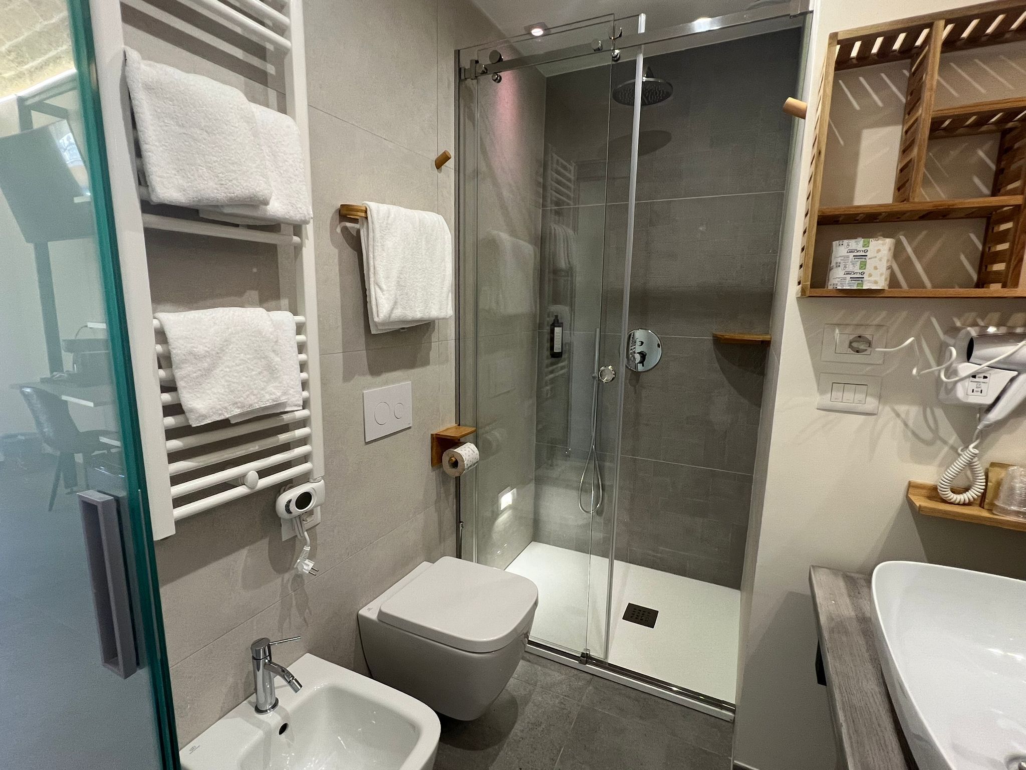 A modern bathroom with a glass-enclosed shower, a toilet, a sink, and a towel rack with multiple towels.
