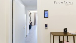 Un pasillo con una puerta, un panel de control en la pared y una pequeña mesa con un libro y una tarjeta.