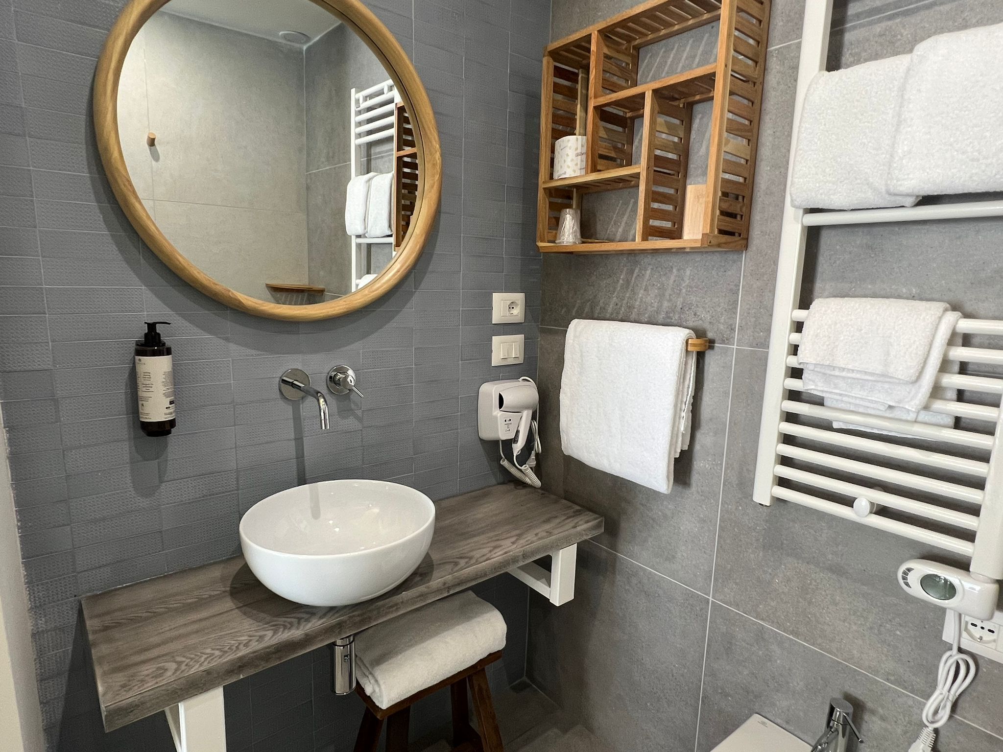 A modern bathroom with a round mirror, a wooden vanity, a white sink, a towel rack, and a built-in heater.