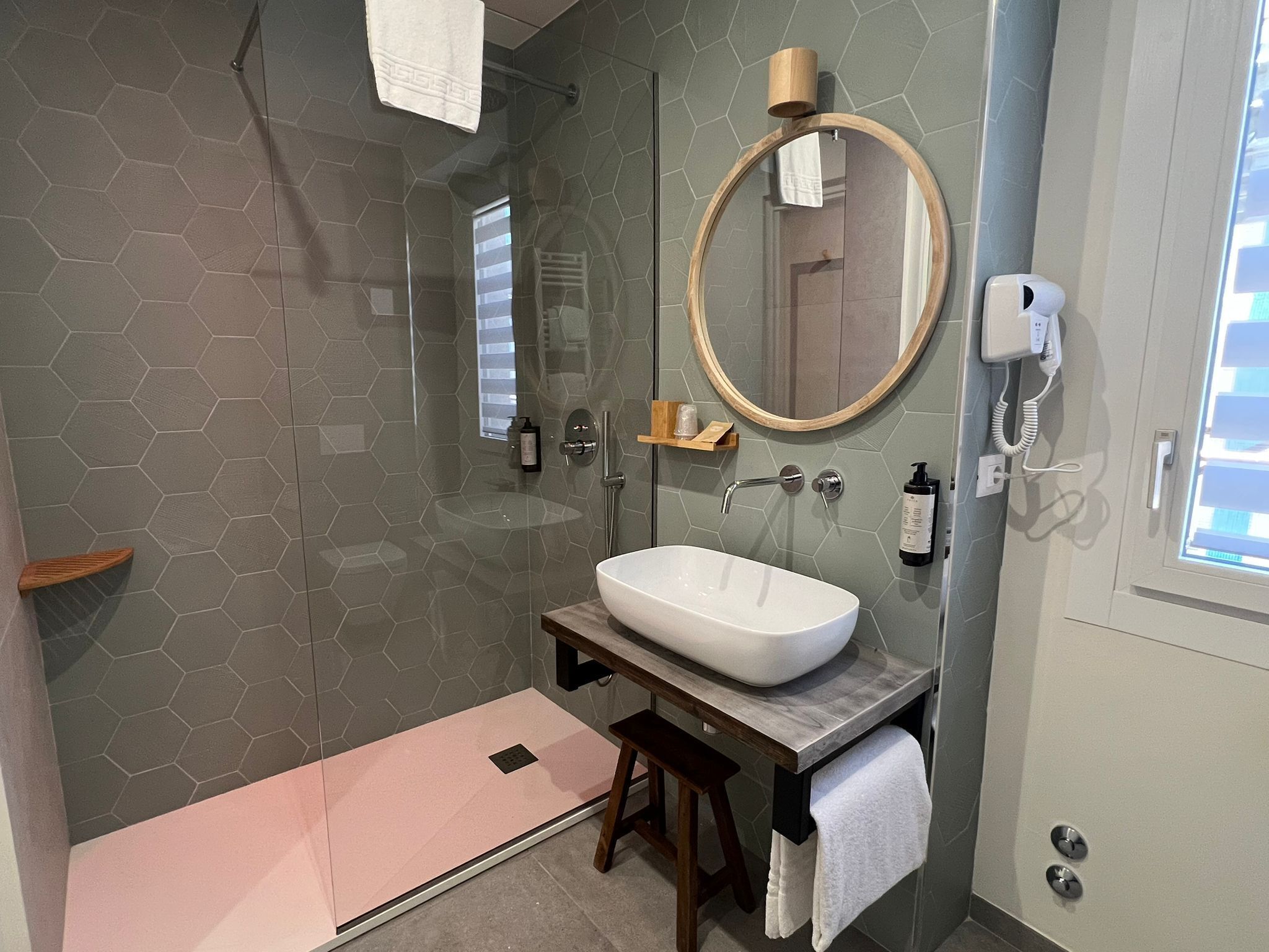 A modern bathroom with a hexagonal tile wall, a large round mirror, a white sink, and a handheld showerhead.