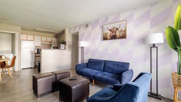 A modern living room with a blue sofa, two brown ottomans, and a dining area with a wooden table and chairs.