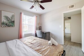 Une chambre à coucher comprenant un lit, un bureau, une chaise, un ventilateur de plafond et une porte donnant sur une autre pièce.