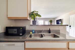 Une cuisine équipée d’un four à micro-ondes, d’un évier à deux bacs et de plantes en pot.