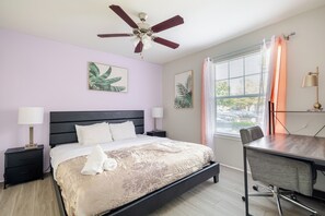 Une chambre à coucher comprenant un lit, un bureau, une chaise, un ventilateur de plafond et deux lampes fixées au mur.