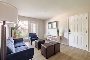 Un salon moderne comprenant un canapé, un pouf, un fauteuil et un téléviseur fixé au mur.
