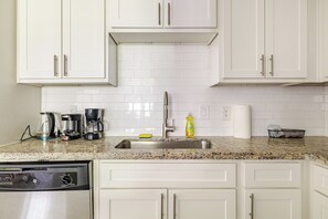 A kitchen with white cabinets, a granite countertop, a dishwasher, a coffee maker, a coffee pot, a dish soap bottle, and a paper towel holder. - Central 3bed 2bath, 5 min Walk to NRG, near MDC (Houston)