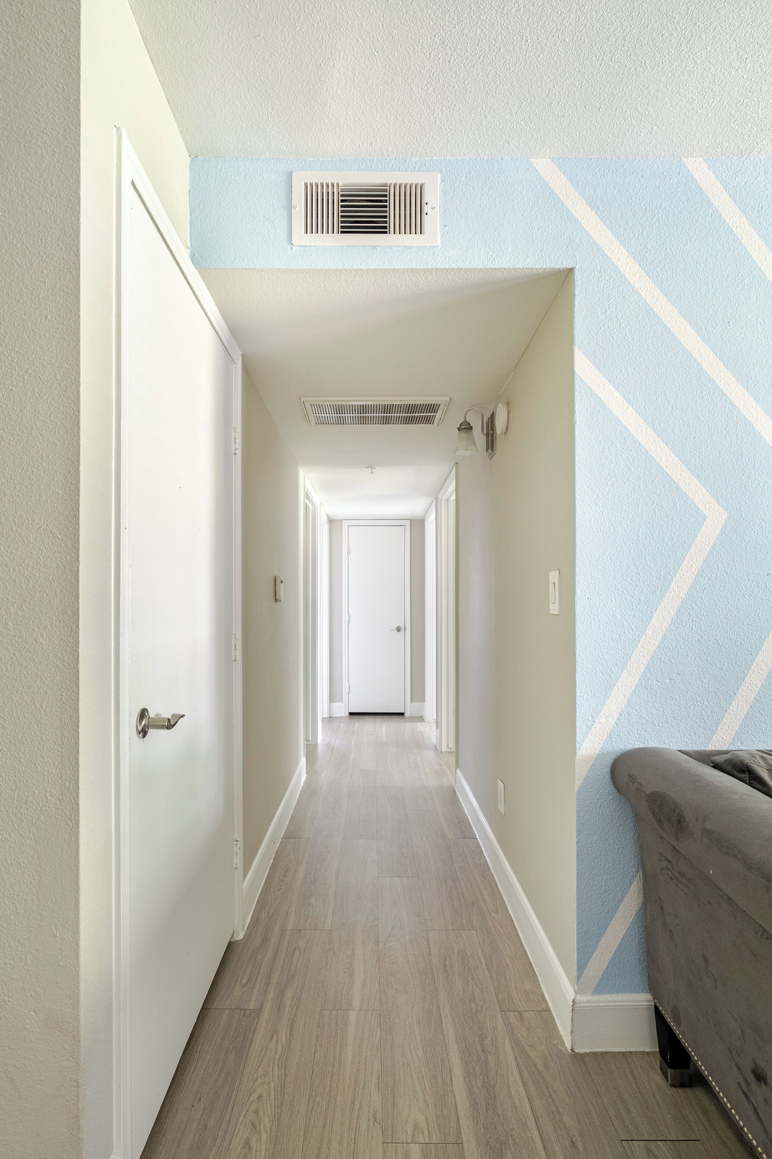 A hallway with a wooden floor, a white door, and a blue wall with a geometric pattern.