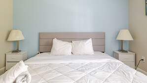 Una cama bien tendida con sábanas blancas, dos mesitas de noche con lámparas y una pared azul claro.