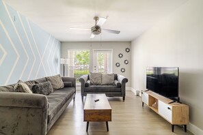 A living room with a sofa, armchair, coffee table, and a TV on a stand.