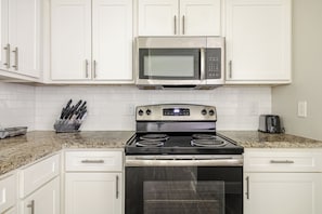 A kitchen with white cabinets, a stainless steel microwave, a gas stove, and a toaster.
