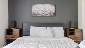 Un dormitorio con una cama, dos mesitas de noche, una pared gris y un cuadro de un árbol.