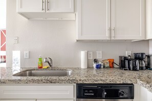 A kitchen with white cabinets, a granite countertop, a dishwashing machine, and various kitchen items.