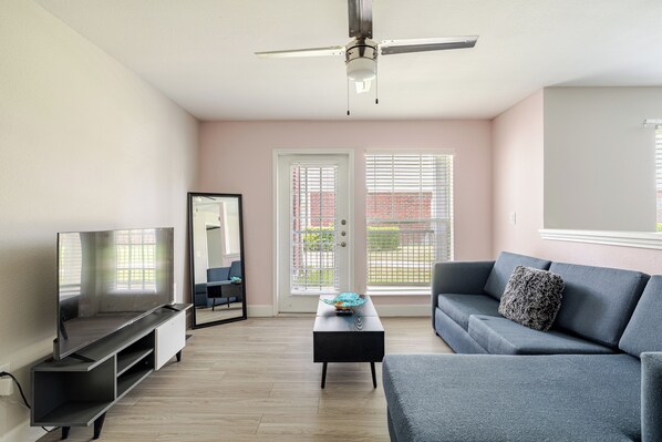 A modern living room with a flat-screen TV, a sofa, a coffee table, and a ceiling fan.